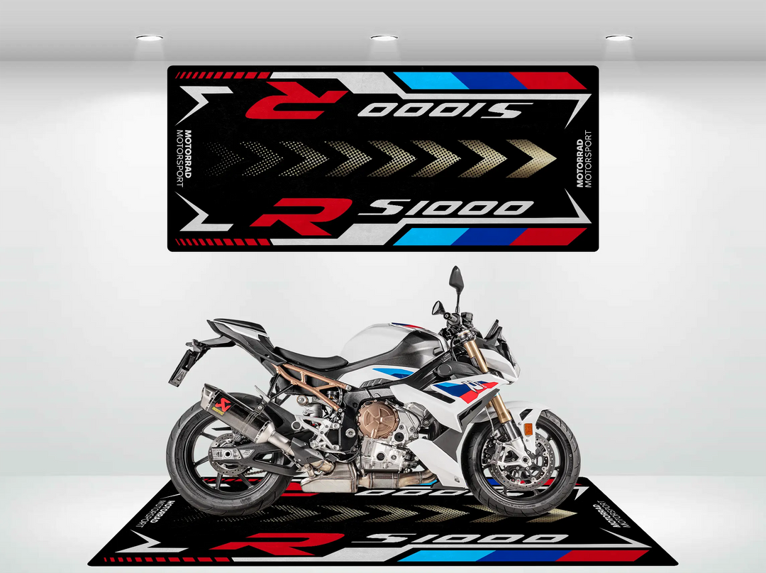 A sleek, sporty motorcycle featuring a white, red, blue, and black color scheme stands proudly on the Motorcycle Pit Mat for S1000R. The wall behind echoes its dynamic design with similar graphics.