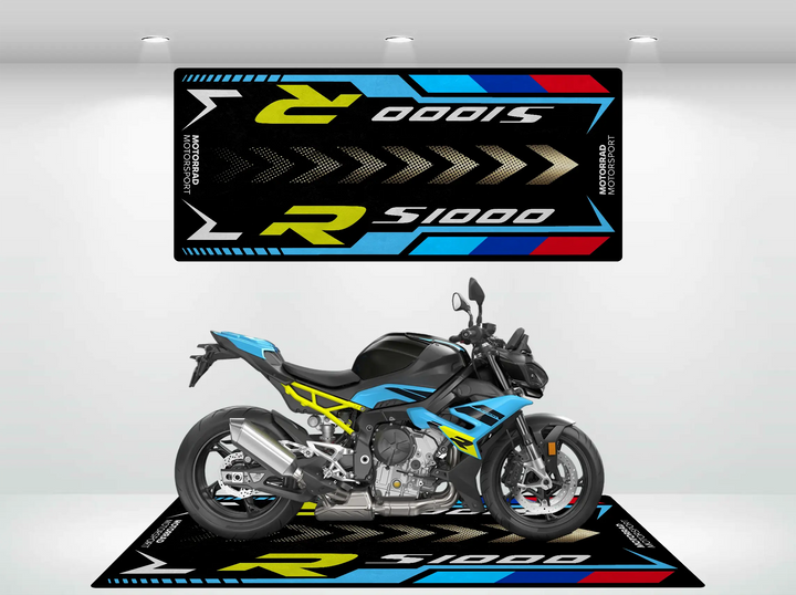 A blue and black motorcycle is showcased with matching wall and floor graphics, featuring a custom Motorcycle Pit Mat. The mats design includes yellow and white chevrons with bold S1000R lettering, merging style with function.