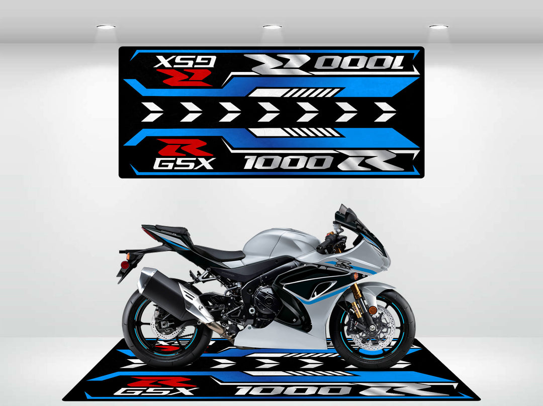 A sleek, silver and black motorcycle is displayed on a stylish Motorcycle Pit Mat, designed for the Suzuki GSX - R1000R 2025. Above it, a wall panel in matching blue and white geometric patterns shows off the XGS 1000 R GSX text in a well-lit showroom.