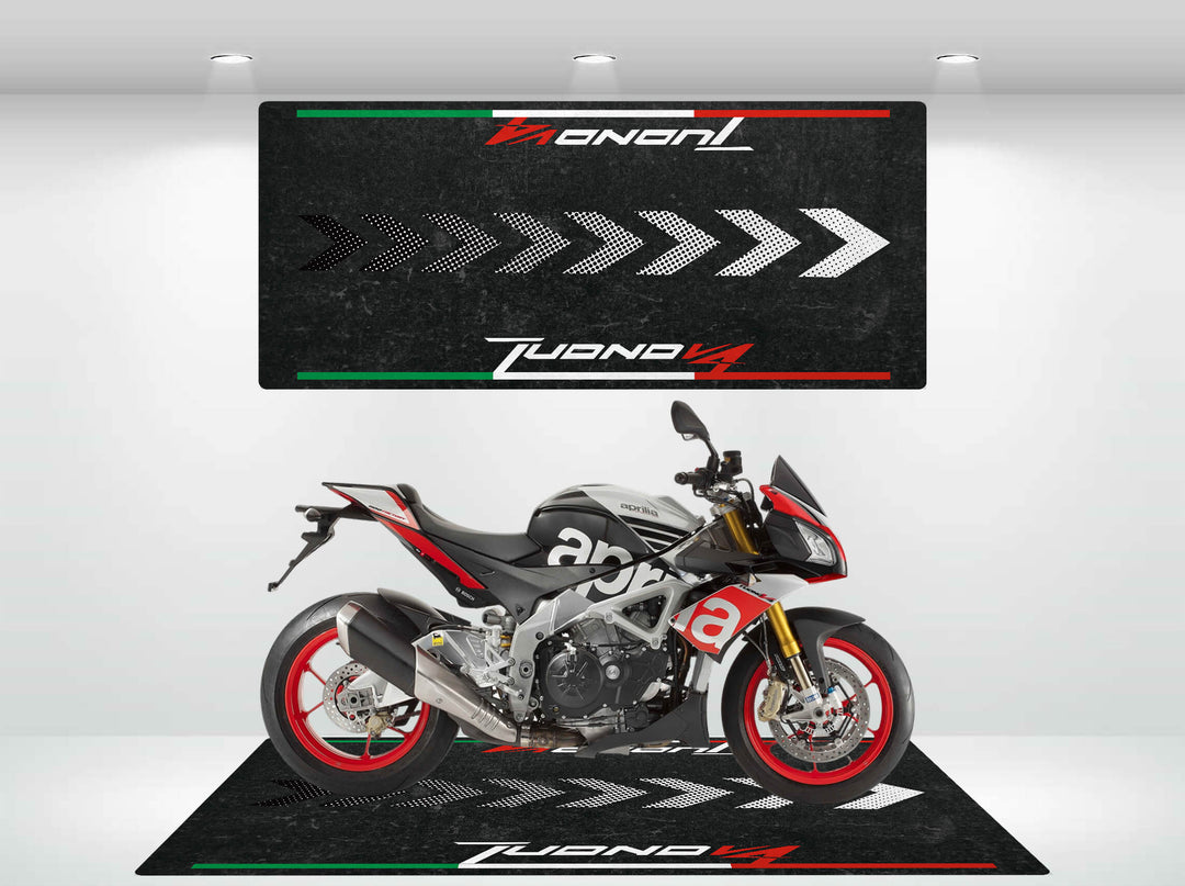 A sleek motorcycle with red and black accents is showcased indoors on a stylish Motorcycle Pit Mat, designed for the Tuono V4 Italian. The wall and floor share a matching design with white arrows and Tuono V4, accented by green, white, and red stripes.