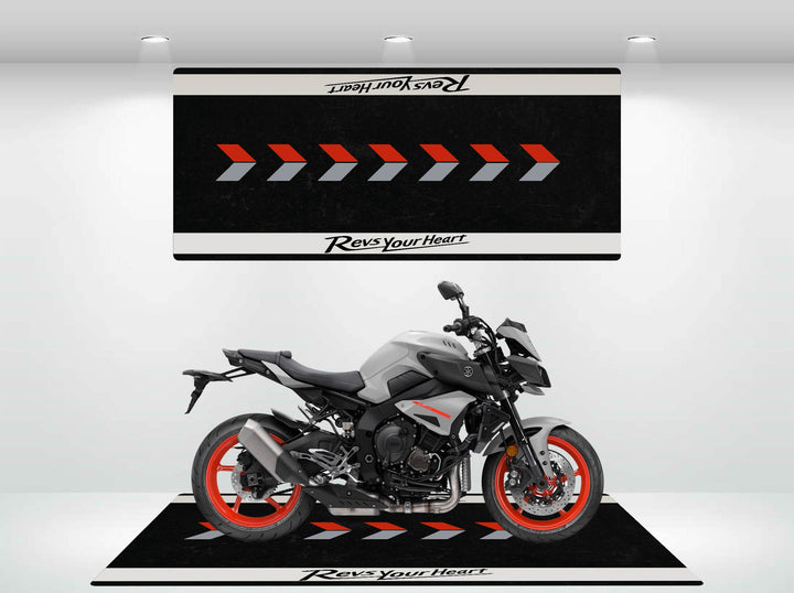 A sleek gray motorcycle with red accents sits on a Motorcycle Pit Mats Yamaha Universal mat, surrounded by geometric patterns and Revs Your Heart text, under well-placed spotlights.