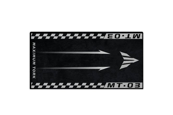 The Motorcycle Pit Mat for Yamaha MT-03 is a black and gray rectangle featuring MAXIMUM TORK and MT.03 on the edges, two upward arrows, and a stylized triangle logo. The textured background gives it a rugged look.