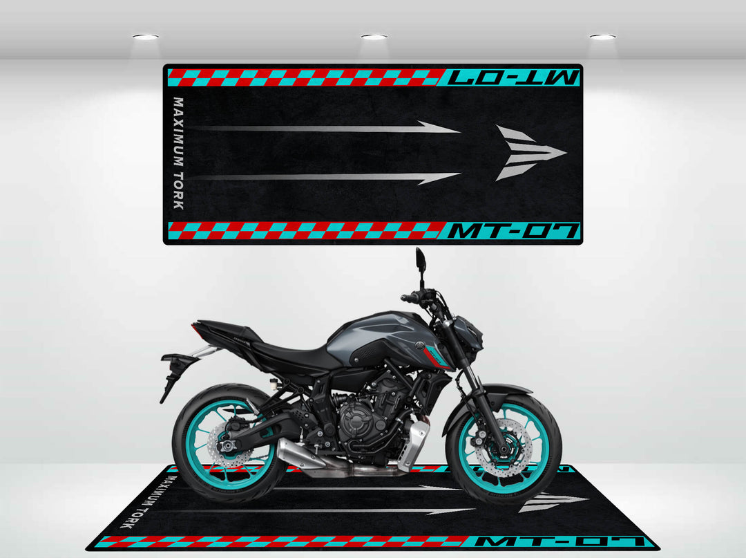 A sleek black motorcycle with turquoise wheels is showcased on a Yamaha MT-07 motorcycle mat from Motorcycle Pit Mat in a modern showroom, featuring a racing-themed design with red and turquoise checkerboards, arrows, and MT-07 Maximum Torque text.