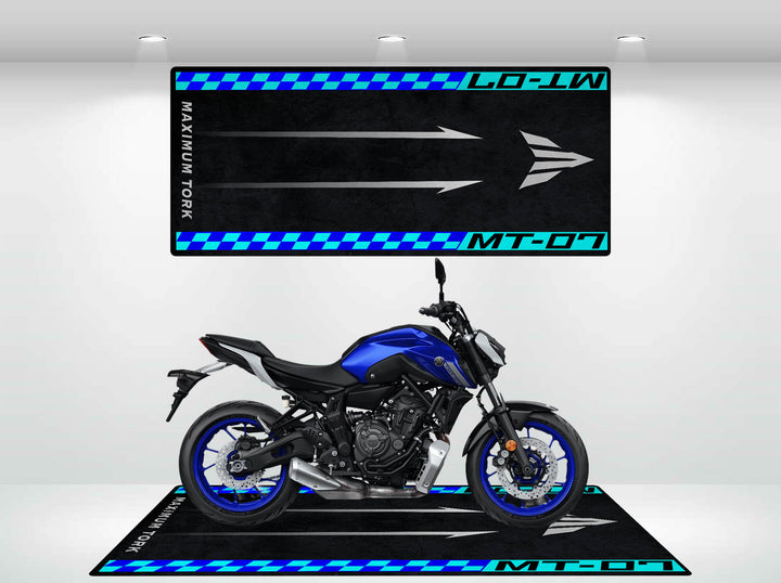 In a showroom, a blue motorcycle rests on a Motorcycle Pit Mat emblazoned with checkered patterns and MAXIMUM TORQUE alongside MT-07. Bright overhead lights enhance the scene.