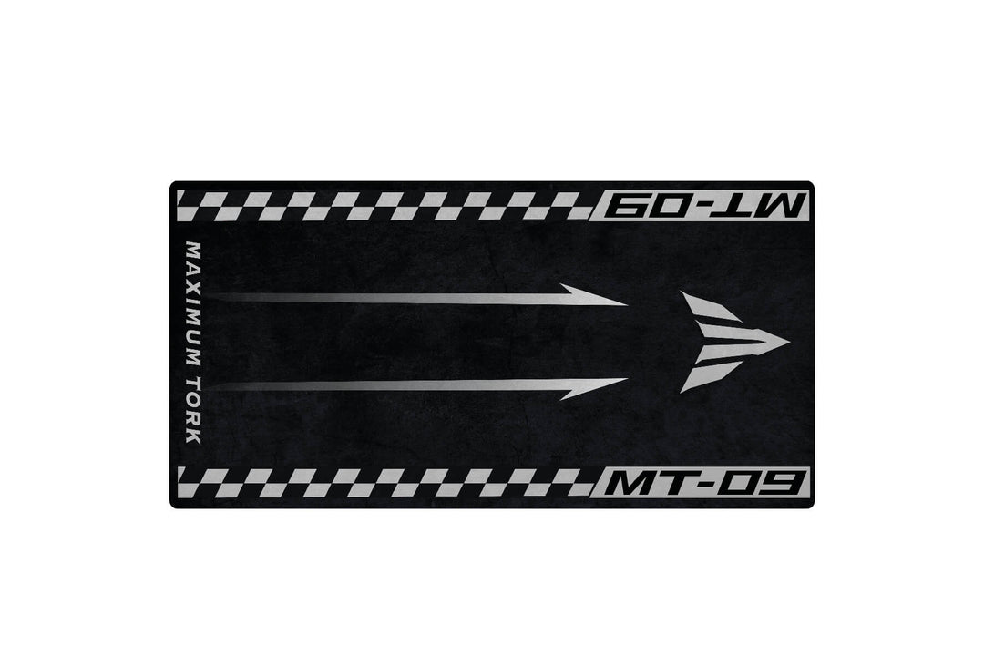 The Motorcycle Mat for Yamaha MT-09 by Motorcycle Pit Mat features a black and gray design with three right-pointing arrows, bordered by a checkered race flag pattern. It includes the text Maximum Tork and MT-09, perfect for any motorbike corner or garage setup.