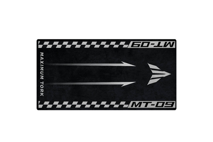 The Motorcycle Mat for Yamaha MT-09 by Motorcycle Pit Mat features a black and gray design with three right-pointing arrows, bordered by a checkered race flag pattern. It includes the text Maximum Tork and MT-09, perfect for any motorbike corner or garage setup.