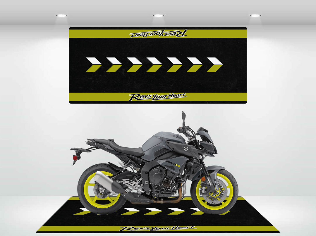 A sleek gray motorcycle with yellow wheels sits on a stylish Motorcycle Pit Mat designed for Yamaha, featuring black and yellow chevrons, in a showroom. A matching sign above reads Revs Your Heart.