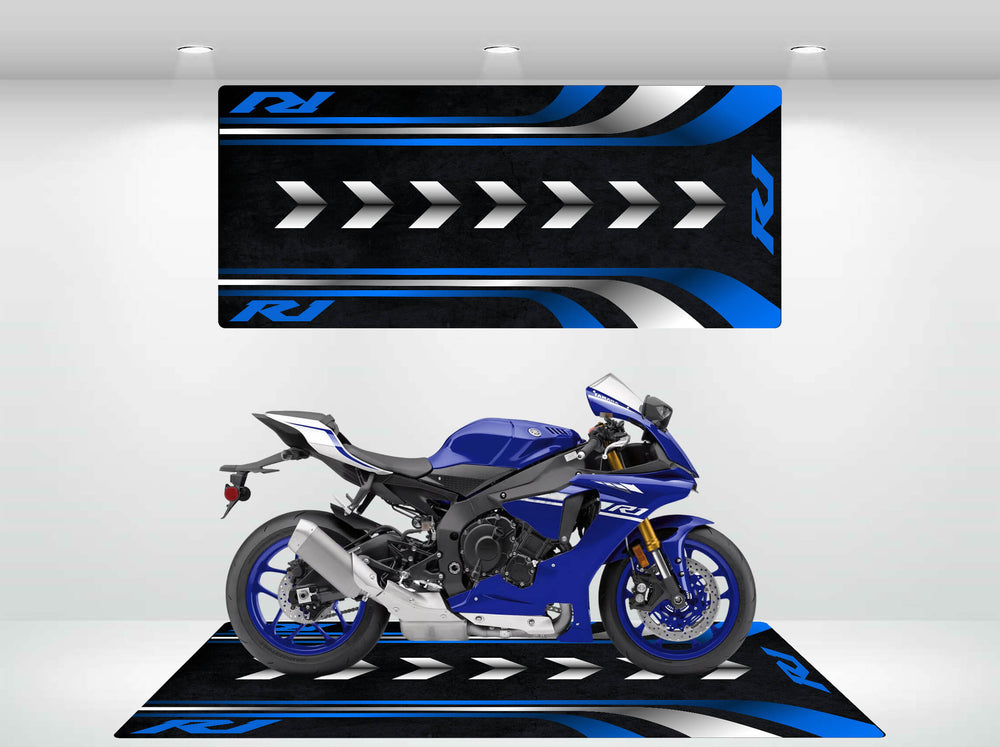 A Yamaha R1 motorcycle sits on a matching Motorcycle Pit Mat in blue, black, and white with arrow designs. The setup includes a back panel and floor mat complemented by overhead lighting.