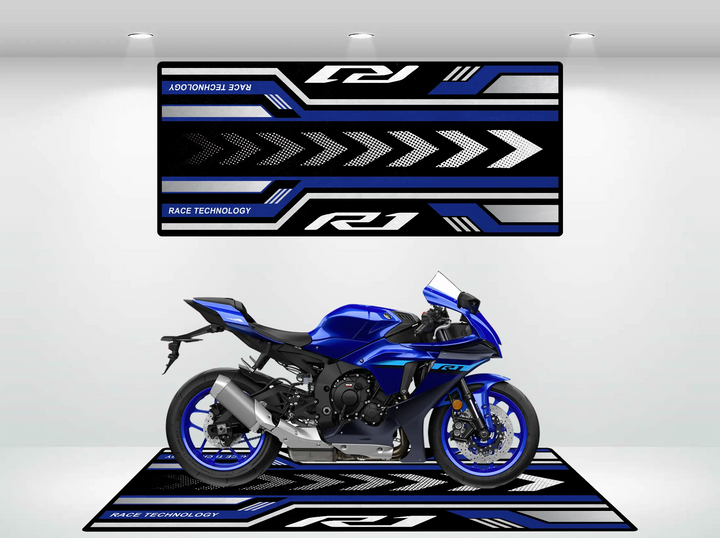 A Yamaha R1 2025 blue and black motorcycle is displayed on a decorative Motorcycle Pit Mat, featuring geometric patterns with arrows in black, white, and blue. The words RACE TECHNOLOGY and R1 are shown on both the motorbike mat and matching wall panel.