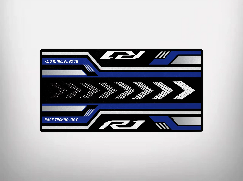 The Motorcycle Pit Mat for Yamaha R1 2025 features a racing geometric design with bold black, blue, and white stripes, stylized arrows, and Race Technology text—a perfect addition to any motorcycle garage collection.