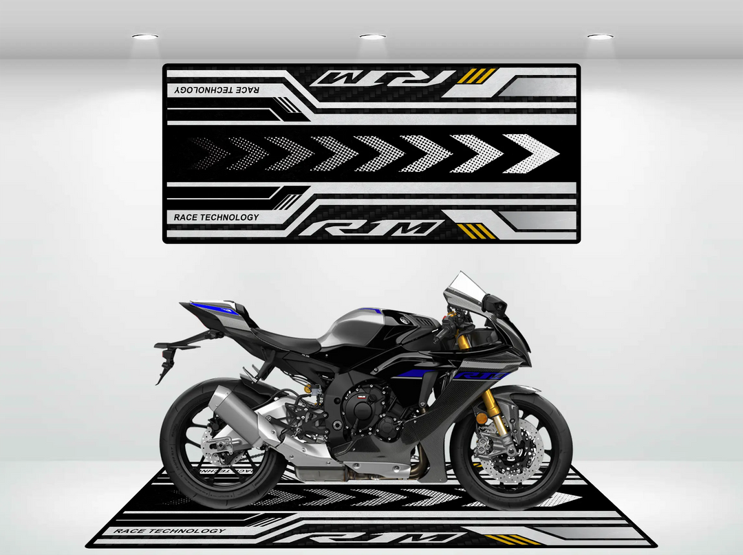 A Yamaha R1M 2025 stands on a black and blue Motorcycle Pit Mat with white and gray arrows. Above, a wall mat echoes the design with RACE TECHNOLOGY and RM. Bright lights illuminate this setup.