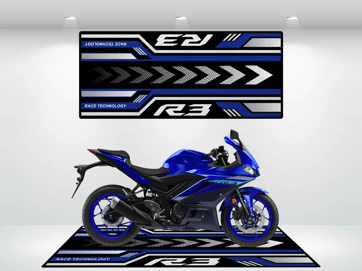 A Yamaha R3 2025 sports motorcycle sits on a blue, black, and white Motorcycle Pit Mat in the showroom. Above it, a decorative panel displays racing graphics and the phrase Race Technology.