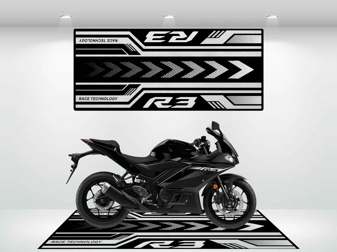 A sleek black motorcycle is showcased on a 2025 Yamaha R3 Motorcycle Pit Mat in a showroom, with a backdrop of black and white geometric designs featuring Race Technology and R3. Spotlights illuminate every detail.