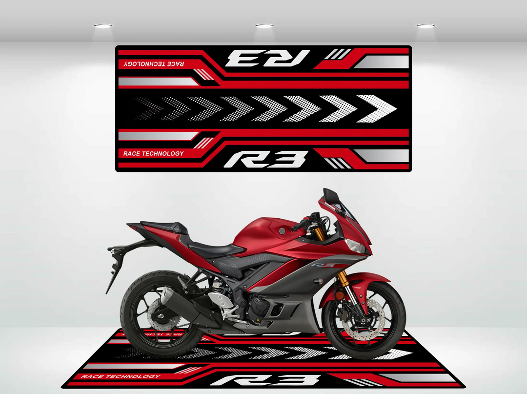 A red sport motorcycle rests on a Yamaha R3 2025 mat from Motorcycle Pit Mat, showcasing red, black, and white geometric designs with arrows. Above it, a matching banner displays Race Technology R3, echoing the dynamic patterns of this stylish setup.