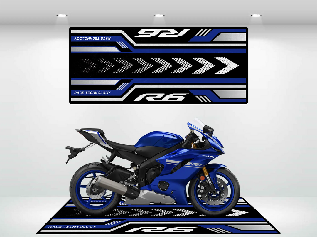 A blue sport motorcycle is on display in a showroom, parked on a Yamaha R6 Motorcycle Pit Mat featuring blue, black, and white geometric patterns. A matching banner above complements its sleek, aerodynamic design.