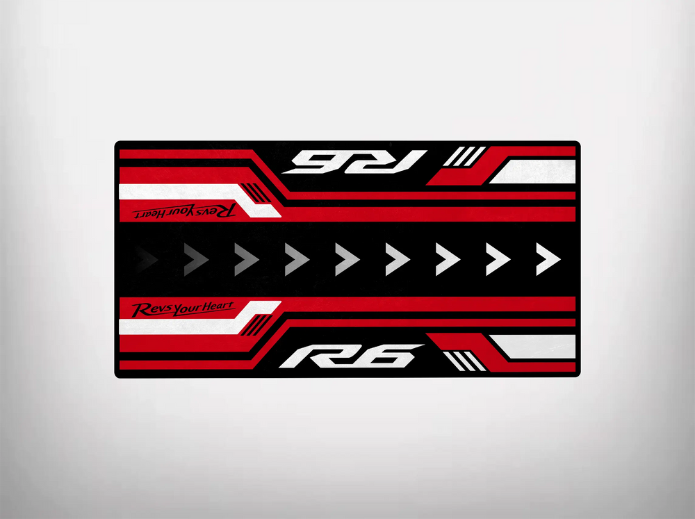 The Motorcycle Pit Mat for Yamaha R6 Vintage is a rectangular garage mat showcasing a bold geometric design in red, black, and white. It prominently features Revs Your Heart and R6 alongside arrow and stripe patterns for a dynamic, racing-inspired appearance.