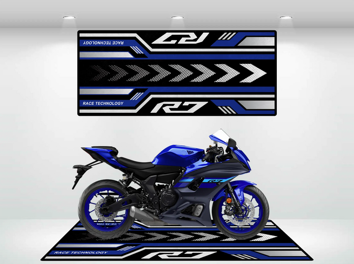 A blue Yamaha R7 motorbike sits on a Motorcycle Pit Mat, with bold arrow graphics and the text Race Technology in the backdrop. The bike gleams under bright lights in a minimalist setting, highlighting its sleek design.