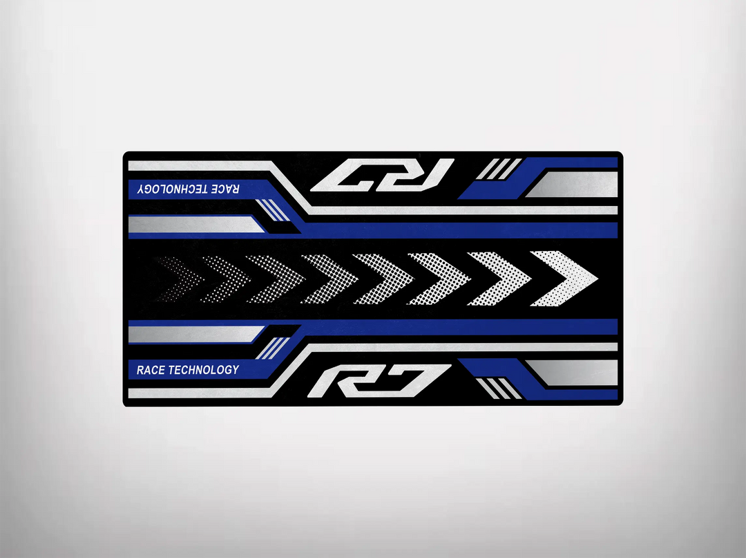 The Motorcycle Pit Mat for Yamaha R7 showcases a geometric pattern with black, blue, and white right-pointing arrows. R7 and Race Technology text in the corners enhance its sleek, modern look for any motorcycle garage.