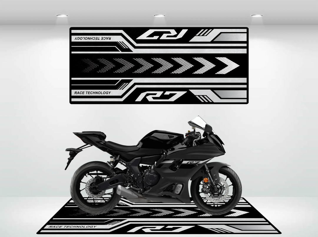 A sleek black Yamaha R6 is showcased on a Motorcycle Pit Mat for Yamaha R7, featuring geometric designs and arrows. The backdrop echoes these patterns with Race Technology in black and white; bright overhead lights enhance the display.