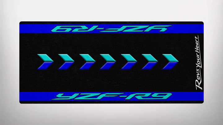 A graphic image of blue and teal geometric arrows on a black background evokes speed, with YZF-R9 boldly displayed. The text Revs Your Heart is vertically aligned on the side. This design is featured on the Motorcycle Pit Mats Motorcycle Mat for Yamaha R9.