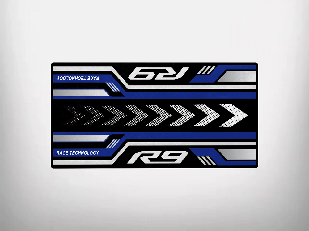 The Motorcycle Pit Mat, perfect for Yamaha R9, features a rectangular racing-themed design with blue, white, and black stripes. Arrows point right alongside the words R9 and RACE TECHNOLOGY, enhanced by angled lines for a dynamic effect—ideal for your motorcycle or garage floor.