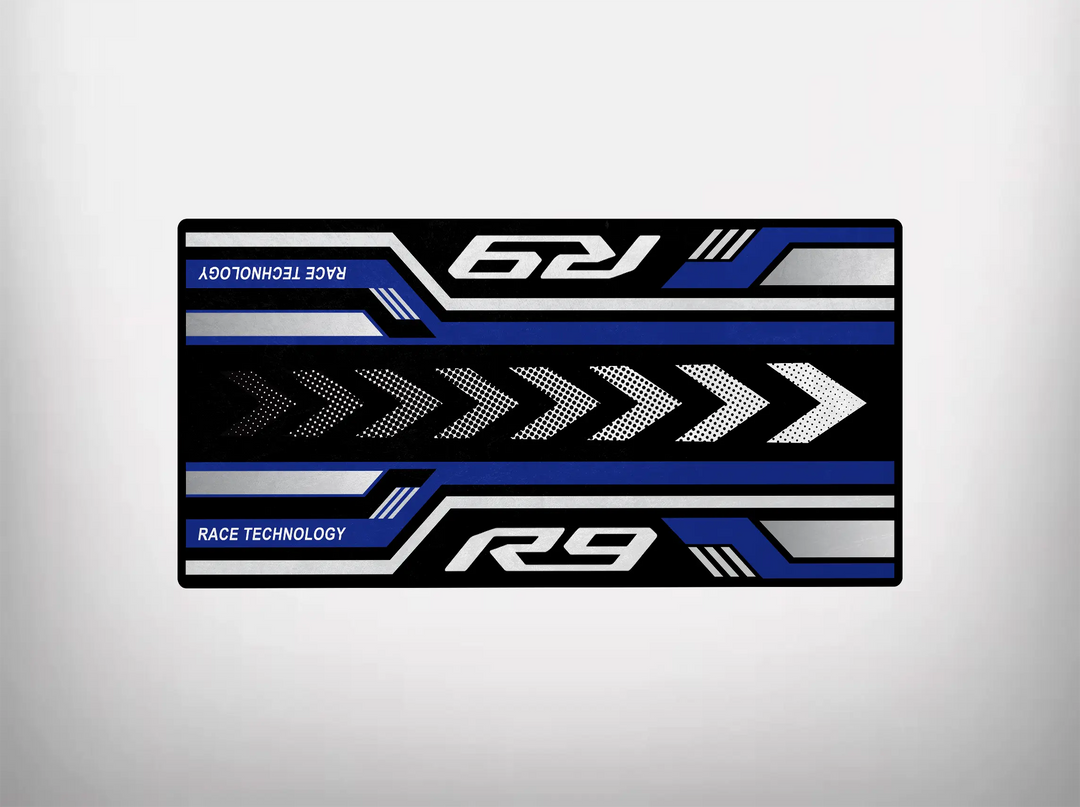 The Motorcycle Pit Mat, perfect for Yamaha R9, features a rectangular racing-themed design with blue, white, and black stripes. Arrows point right alongside the words R9 and RACE TECHNOLOGY, enhanced by angled lines for a dynamic effect—ideal for your motorcycle or garage floor.