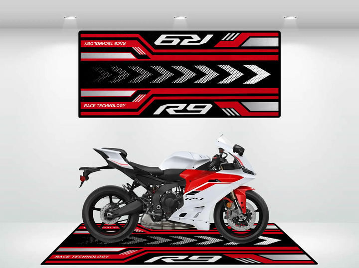 A sleek white sport motorcycle is parked indoors on a Motorcycle Pit Mat for Yamaha R9, featuring bold geometric patterns and R9 and RACE TECHNOLOGY. A matching banner with similar designs hangs on the wall behind it.