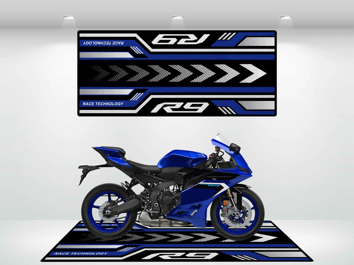 A blue sports motorcycle sits on the Motorcycle Pit Mat for Yamaha R9, enhancing its sleek design with R9 and Race Technology text. The backdrop mirrors these with dynamic arrows and matching text.