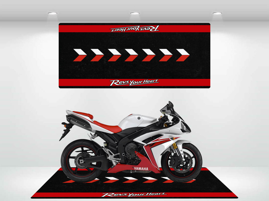 A sleek red and white Yamaha motorcycle is showcased on a Motorcycle Pit Mats Motorcycle Mat for Yamaha Universal in the showroom. It features a backdrop with the text Revs Your Heart and is brightly illuminated by overhead lights.