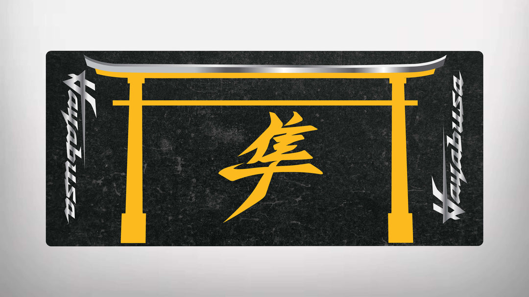 The black rectangular motorcycle mat for Suzuki Hayabusa features a yellow traditional gate design with a stylized symbol center. It has silver metallic text on both sides, creating an elegant and sleek finish, characteristic of the Motorcycle Pit Mat brand.